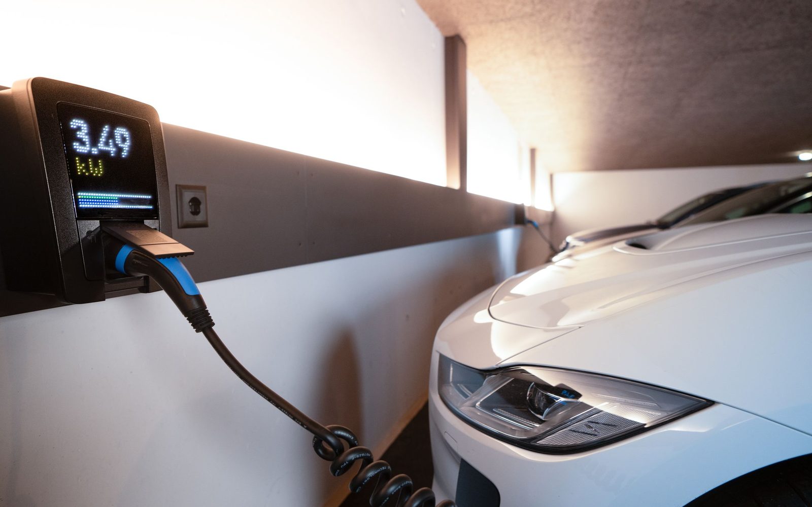 Wallbox an der Garagenwand lädt ein weißes Elektroauto